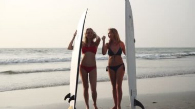 Deniz sahilinde sörf tahtası olan iki kadın bikinili sörfçü.