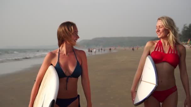 Две молодые женщины в купальниках идут по пляжу с досками для серфинга. Медленное движение — стоковое видео