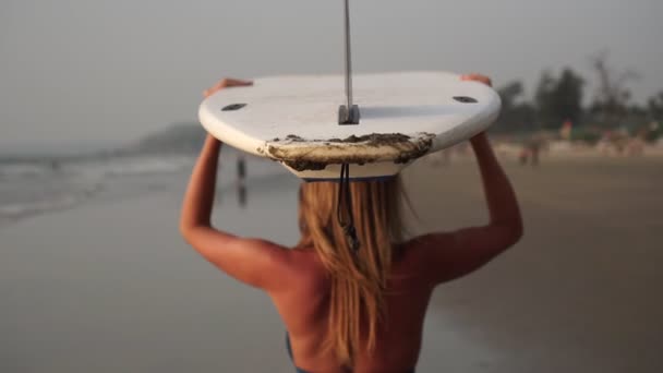 Surfista menina caminha ao longo da praia com uma prancha de surf. Movimento lento — Vídeo de Stock