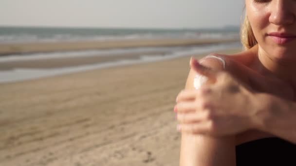 Una donna su una spiaggia in costume da bagno applica la crema solare sulla sua pelle — Video Stock