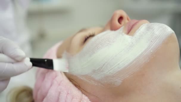 Kosmetolog nanáší krém na kůži ženské tváře. Kosmetika, omlazování. — Stock video