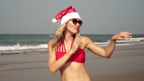 Navidad, una mujer joven en bikini baila en una playa de mar en un sombrero de Año Nuevo — Vídeo de stock