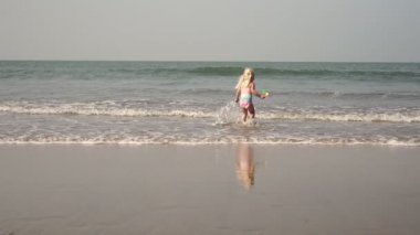 Çocuk plajda oynar ve suya su sıçratır. Çocukluk, deniz, seyahat