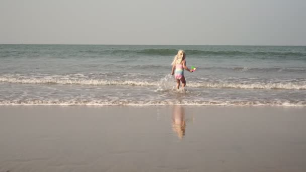 Девочка играет на морском пляже и брызгает в воду. Детство, море, путешествия — стоковое видео