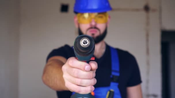 Een mannelijke bouwer houdt een elektrische schroevendraaier vast. Portret van een mannelijke arbeider in uniform. — Stockvideo