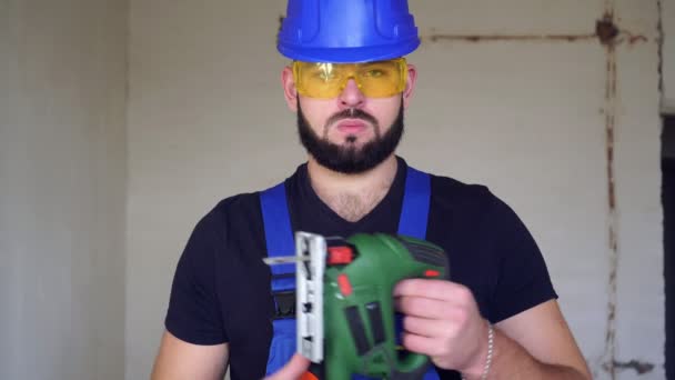 Hombre trabajador con una sierra eléctrica. Retrato de un constructor con un rompecabezas eléctrico — Vídeos de Stock