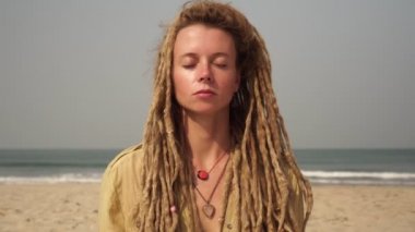 Denizin arka planında meditasyon yaparken rastalı genç bir kadının portresi..