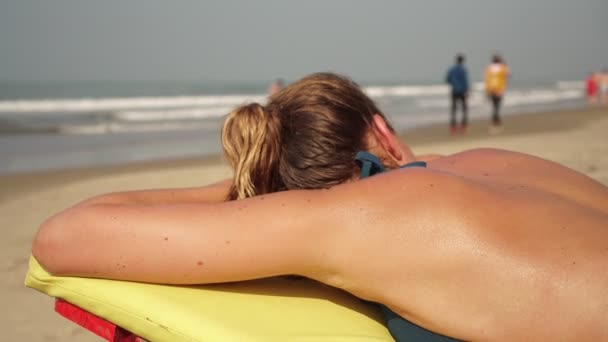 Jovem mulher bonita banhos de sol em uma praia. Menina banhos de sol em uma cadeira de convés — Vídeo de Stock