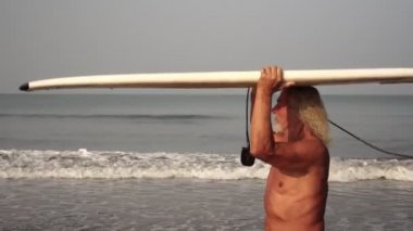 Plajda sörf tahtası olan atletik yaşlı bir adam. Sörf yapan olgun bir adamın portresi.