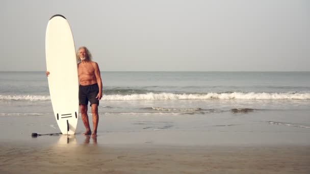 Viejo hombre maduro con una tabla de surf sobre un fondo del mar — Vídeos de Stock