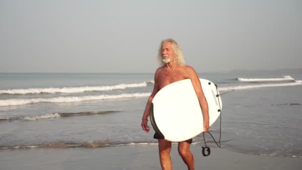 Grand-père avec une planche de surf sur la plage. Vieux surfeur masculin mature — Video