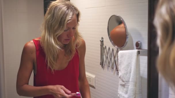 Ung blond kvinna borstar tänderna i badrummet — Stockvideo