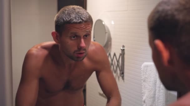 Een jonge slaperige man wast zich in de badkamer voor een spiegel — Stockvideo