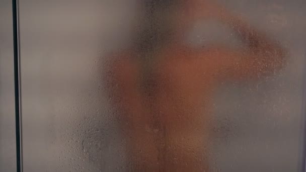 En silhuett av en naken kvinna i duschen bakom ett mistat glas — Stockvideo
