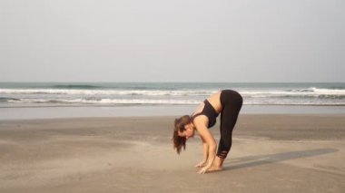 Genç ve güzel bir kadın sahilde yoga yapıyor.