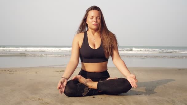 Ragazza medita in posizione di loto vicino al mare. Una giovane donna pratica yoga sulla spiaggia — Video Stock