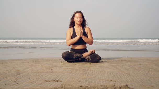 Chica está meditando cerca del mar. Joven hermosa mujer practica yoga en la playa — Vídeo de stock