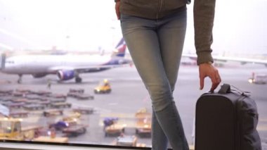Havaalanı terminalinde, uçakların önünde küçük bavullu bir kadın turist.