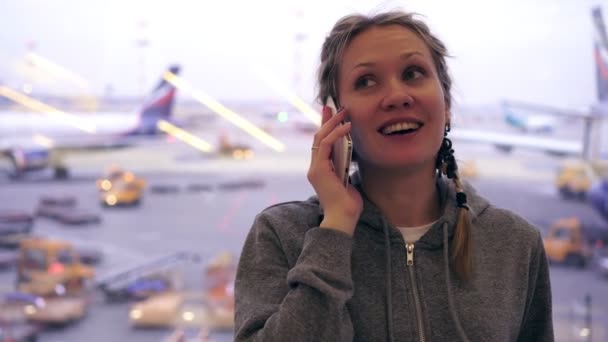 Ung vit kvinna talar i telefon på flygplatsen i bakgrunden av flygplan — Stockvideo