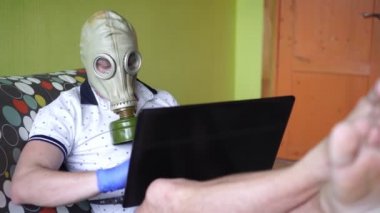 Solunum cihazlı ya da gaz maskeli bir adam evde dizüstü bilgisayarla çalışıyor. Enfeksiyona karşı koruma