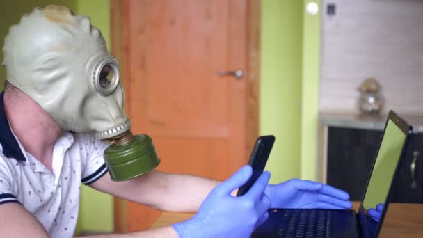 A man in a respirator at home with a laptop and smartphone. Home office and coronovirus — Stock Video