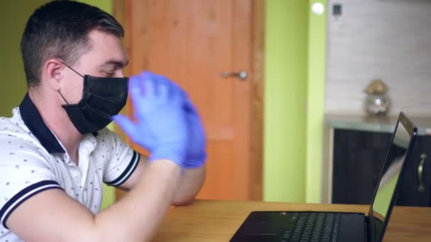 Человек в медицинской маске и перчатках работает дома с ноутбуком — стоковое видео