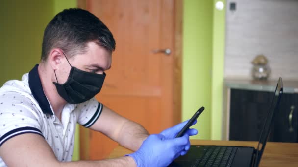 Um homem com um portátil com uma máscara médica. Coronovírus, quarentena, escritório em casa — Vídeo de Stock