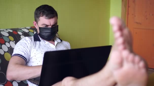 Muž v lékařské masce s laptopem v domě. Coronovirus a domácí kancelář — Stock video