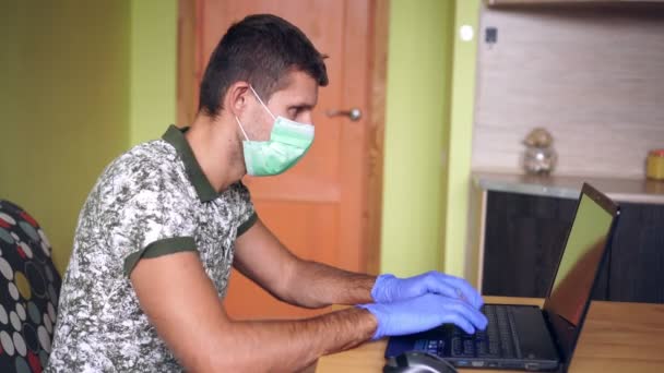 Человек в медицинской маске с ноутбуком в доме. Эпидемия, короновирус и домашний офис — стоковое видео