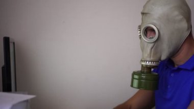 Gaz maskeli bir adam evde bilgisayarla çalışıyor. Karantina, koronovirüs, merkez ofis.
