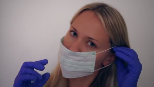 Egy orvosi maszkos nő portréja. Egy fiatal nő orvosi maszkot visel. — Stock videók