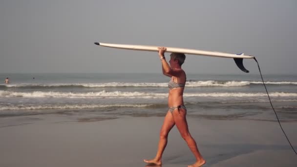 Vuxen mogen kvinna på stranden med en surfbräda. Mormor med en surfing — Stockvideo