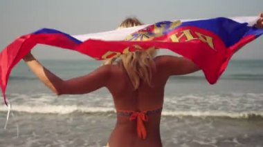 Plajda mayo giymiş genç bir kadın Rus bayrağını taşıyor.