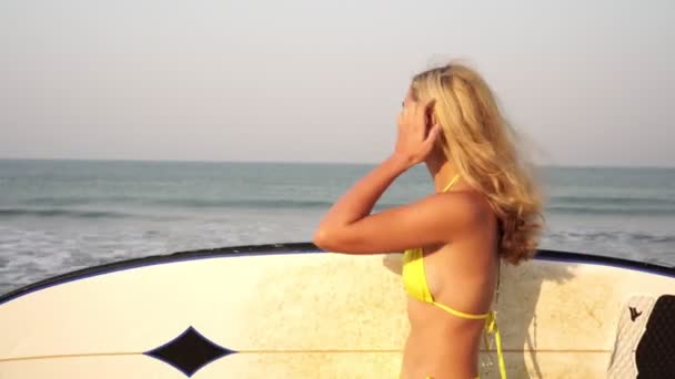 Uma jovem mulher de fato de banho com prancha de surf caminha pelo mar — Vídeo de Stock