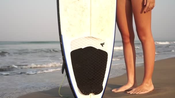 Chica surfista se encuentra en una playa de mar con una tabla de surf. Hermosa mujer con un surf . — Vídeo de stock