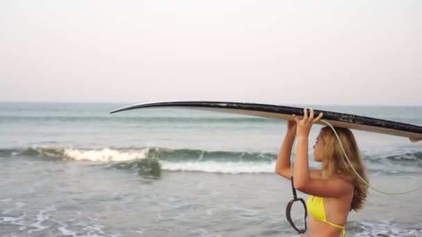 Uma jovem caminha com uma prancha de surf no mar. Menina bonita com um surf — Vídeo de Stock