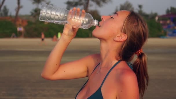 Jonge aantrekkelijke vrouw in een badpak drinkt water uit een fles, slow motion — Stockvideo