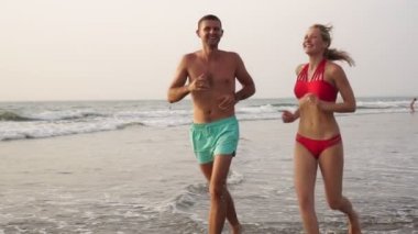 Genç çift aşık, erkek ve kadın plaj ve deniz dalgaları boyunca koşuyor.