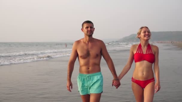 Pareja joven enamorada, hombre y mujer tomados de la mano y caminando por la playa — Vídeo de stock