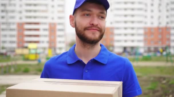 A male courier delivery man with a cardboard box is walking along the street — Stock Video