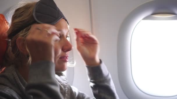 Una pasajera en un avión se pone una venda en los ojos. Chica turista en la cabina del avión — Vídeos de Stock