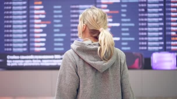 Пассажирка в аэропорту на фоне расписания рейсов — стоковое видео
