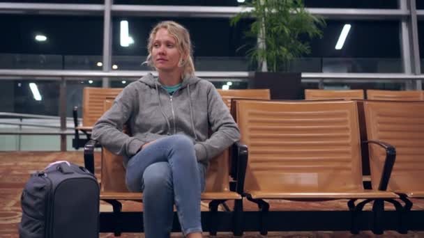 Eine Touristin sitzt am Flughafen und wartet im Terminal auf das Flugzeug — Stockvideo