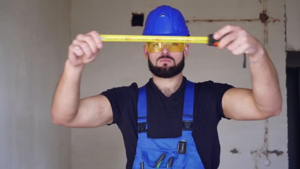 En manlig byggare mäter med en byggtejp. Porträtt av en manlig byggare — Stockvideo