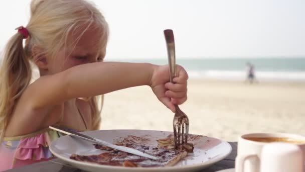 Kind isst Pfannkuchen in einem Café am Strand — Stockvideo