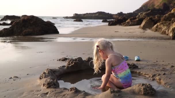 Boldog kislány játszik a homokos tengerparton, közel a tengerhez. Tengerpart, gyermekkor, nyaralás — Stock videók