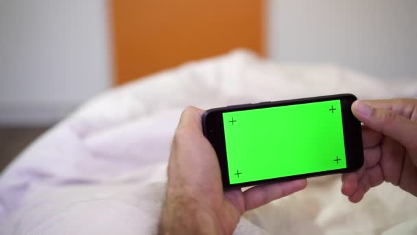 Mano sostiene el teléfono inteligente con pantalla verde en blanco. Un hombre usa un teléfono con una pantalla verde — Vídeos de Stock