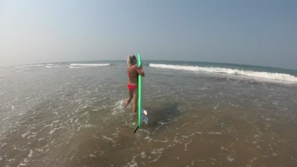 Chica surfista entra en el mar con una tabla de surf. Surf en Goa, India — Vídeos de Stock