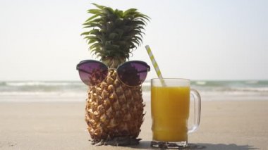 Sahilde güneş gözlüklü ananas ve bir bardak meyve suyu.