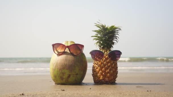 Coco e abacaxi em óculos de sol em uma praia tropical. Conceito de umas férias de praia — Vídeo de Stock